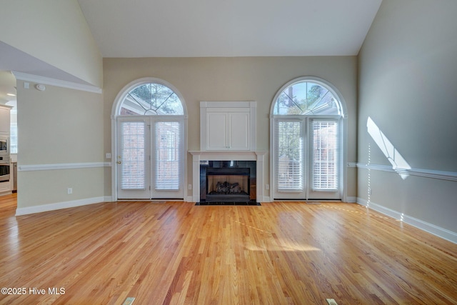 unfurnished living room featuring light wood-style floors, a tile fireplace, high vaulted ceiling, and baseboards