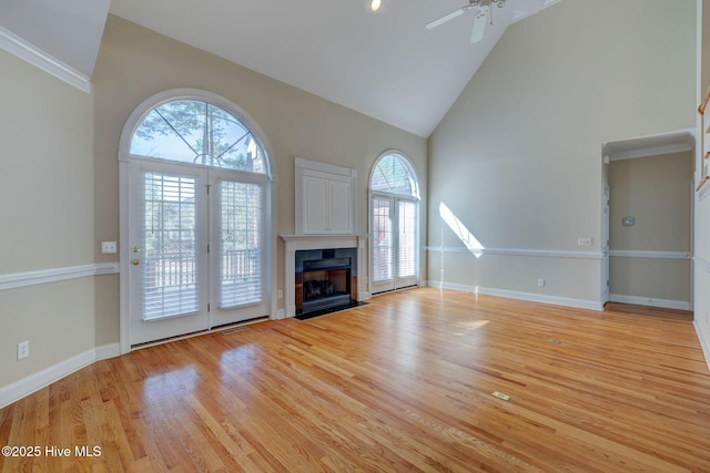 unfurnished living room with baseboards, a fireplace with flush hearth, ceiling fan, light wood-style floors, and high vaulted ceiling