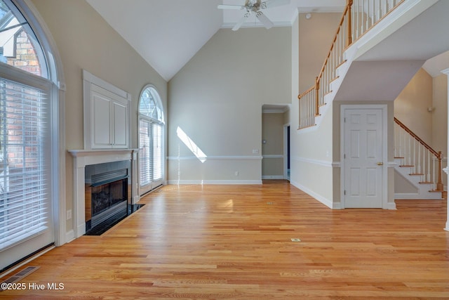 unfurnished living room featuring high vaulted ceiling, light wood finished floors, a tiled fireplace, and stairs