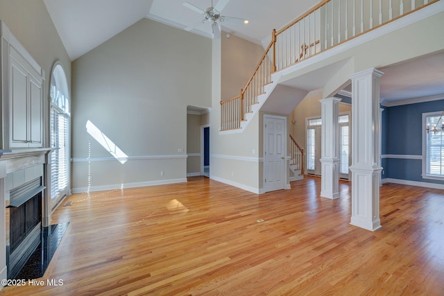 unfurnished living room with a tiled fireplace, light wood finished floors, ornate columns, and ceiling fan