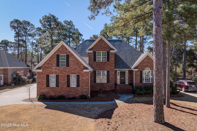 traditional-style home featuring roof with shingles and brick siding