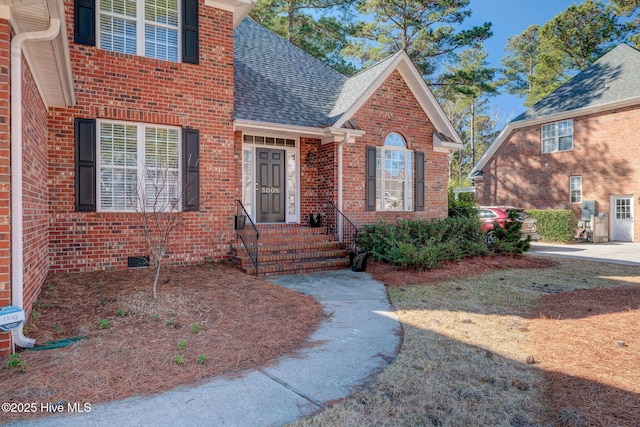 entrance to property featuring a shingled roof and brick siding