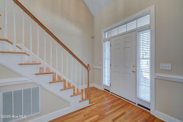 entrance foyer with stairs, visible vents, vaulted ceiling, and wood finished floors