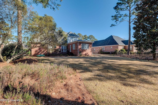 exterior space with a front yard, brick siding, fence, and a wooden deck