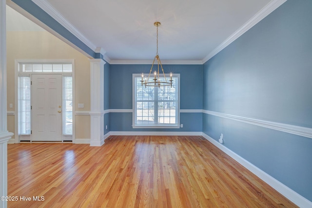 interior space with baseboards, light wood-style floors, ornamental molding, decorative columns, and an inviting chandelier