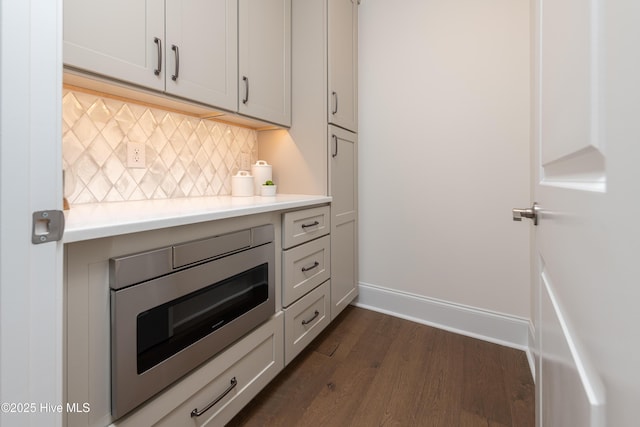 kitchen with stainless steel microwave, white cabinets, dark hardwood / wood-style flooring, and decorative backsplash