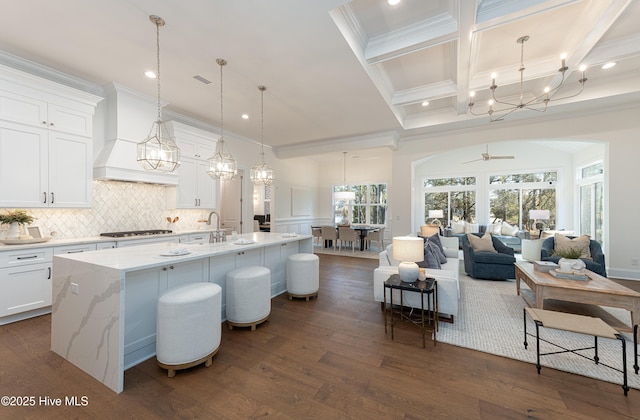 kitchen featuring pendant lighting, light stone counters, an island with sink, white cabinets, and custom exhaust hood