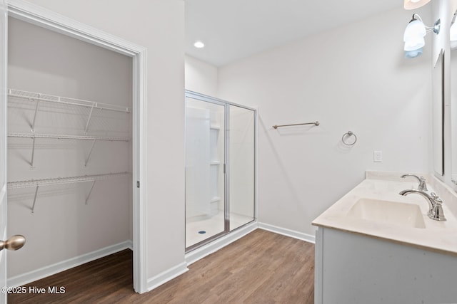 full bath featuring wood finished floors, a sink, baseboards, a spacious closet, and a shower stall