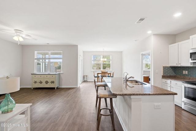 kitchen with a sink, dark wood-style floors, appliances with stainless steel finishes, decorative backsplash, and dark stone counters