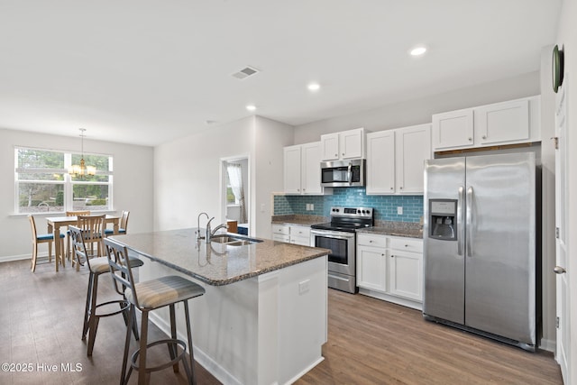 kitchen with stainless steel appliances, a sink, white cabinetry, backsplash, and dark stone countertops