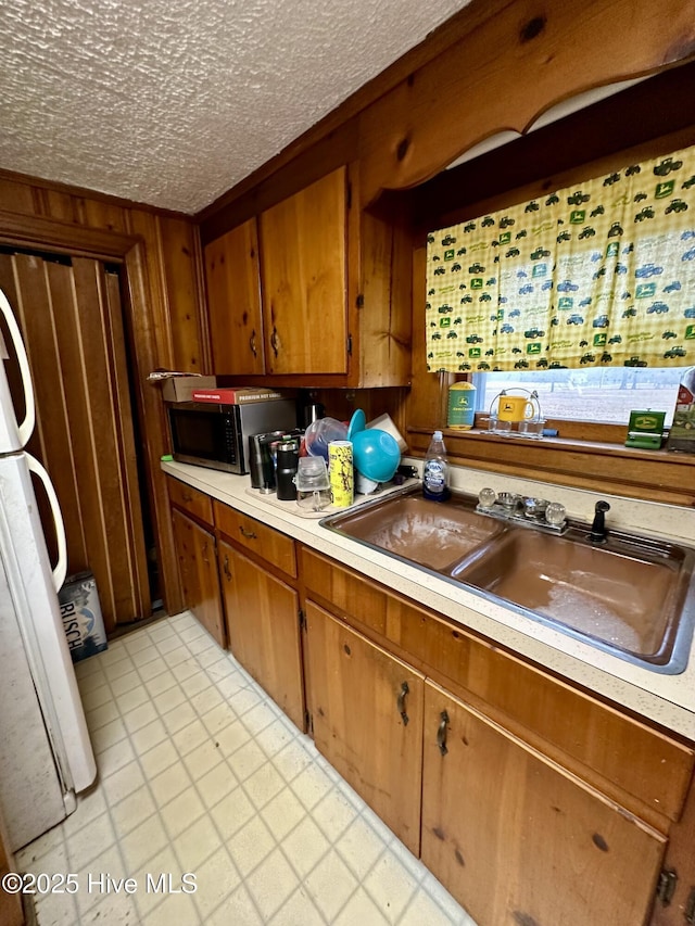 kitchen featuring sink, wood walls, a textured ceiling, and white fridge