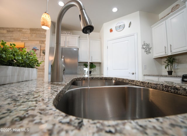 kitchen with tasteful backsplash, white cabinets, light stone counters, pendant lighting, and recessed lighting