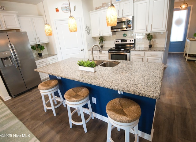 kitchen with a breakfast bar, stainless steel appliances, white cabinets, a sink, and an island with sink