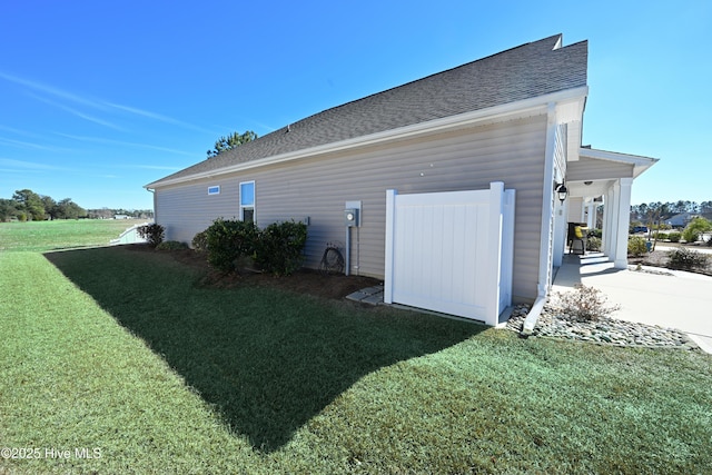 view of side of property with a shingled roof and a lawn