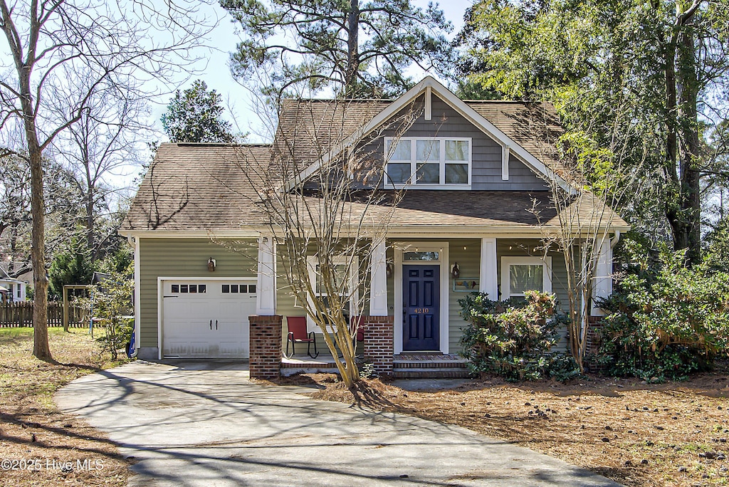 craftsman-style house with a shingled roof, concrete driveway, brick siding, and an attached garage