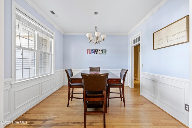 dining room with visible vents, a wainscoted wall, ornamental molding, light wood-type flooring, and a chandelier