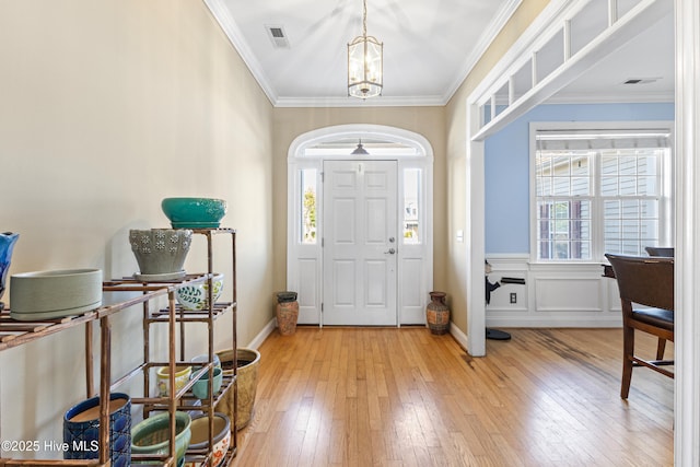 entryway featuring a notable chandelier, visible vents, baseboards, ornamental molding, and light wood finished floors