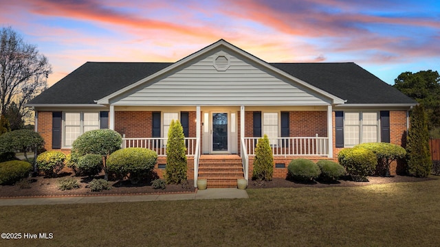 view of front of house featuring brick siding, a porch, a front lawn, and roof with shingles