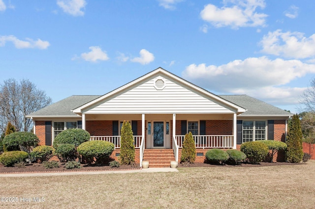 view of front of property featuring brick siding, a porch, a front yard, and roof with shingles