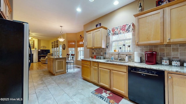 kitchen featuring sink, light stone counters, hanging light fixtures, stainless steel fridge, and black dishwasher