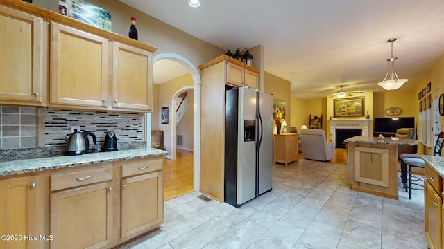 kitchen featuring light brown cabinetry, stainless steel fridge with ice dispenser, backsplash, and hanging light fixtures