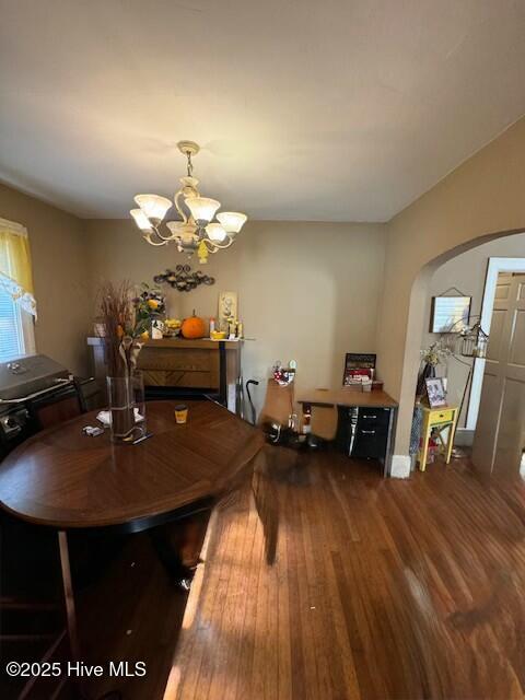 dining area with arched walkways, wood finished floors, and an inviting chandelier