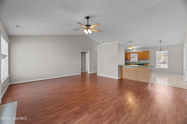 unfurnished living room featuring ceiling fan with notable chandelier, vaulted ceiling, dark hardwood / wood-style flooring, and a textured ceiling