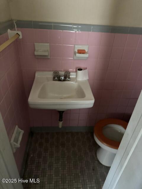 half bath featuring tile walls, toilet, a wainscoted wall, and a sink