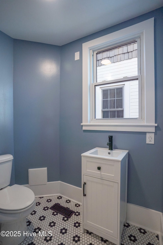 half bathroom with tile patterned flooring, baseboards, vanity, and toilet