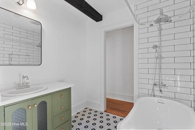 bathroom with a soaking tub, vanity, beam ceiling, and baseboards