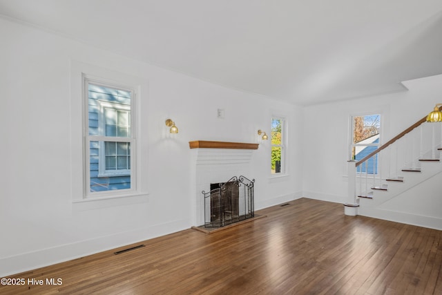 unfurnished living room featuring a brick fireplace, wood finished floors, baseboards, and stairs