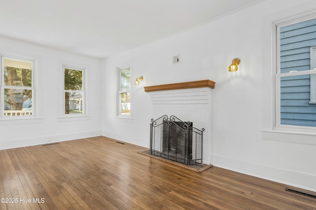 unfurnished living room featuring a brick fireplace, visible vents, baseboards, and wood finished floors