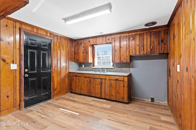 kitchen with wooden walls, light hardwood / wood-style floors, sink, and decorative backsplash