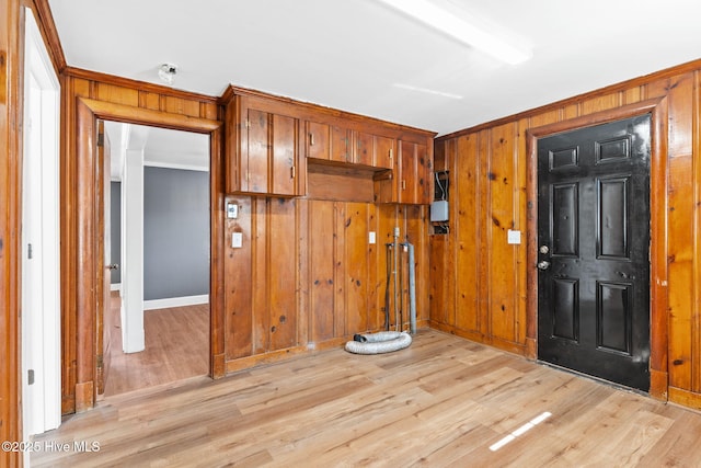 interior space with ornamental molding, wooden walls, and light hardwood / wood-style floors