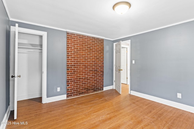 unfurnished bedroom featuring crown molding, a closet, brick wall, and light wood-type flooring