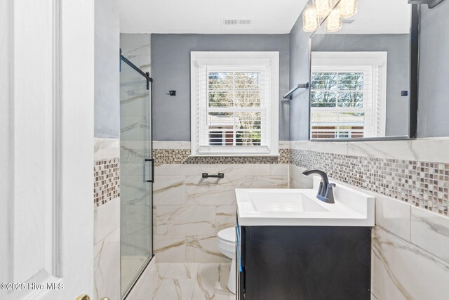 bathroom with vanity, toilet, an enclosed shower, and tile walls