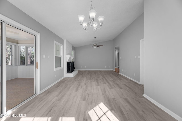 unfurnished living room with light wood finished floors, a fireplace with raised hearth, vaulted ceiling, baseboards, and ceiling fan with notable chandelier