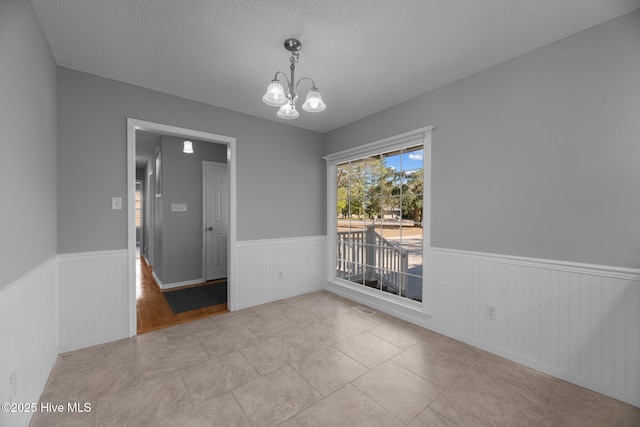 unfurnished dining area featuring a wainscoted wall, visible vents, a chandelier, and a textured ceiling