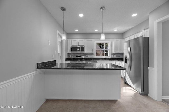 kitchen with a wainscoted wall, a peninsula, stainless steel appliances, white cabinetry, and pendant lighting