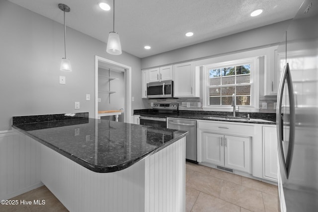 kitchen with a peninsula, a sink, white cabinets, appliances with stainless steel finishes, and decorative light fixtures