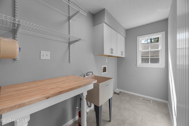 laundry room with hookup for a washing machine, visible vents, light tile patterned flooring, a textured ceiling, and baseboards