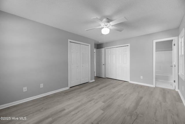 unfurnished bedroom featuring a textured ceiling, connected bathroom, baseboards, light wood-style floors, and two closets