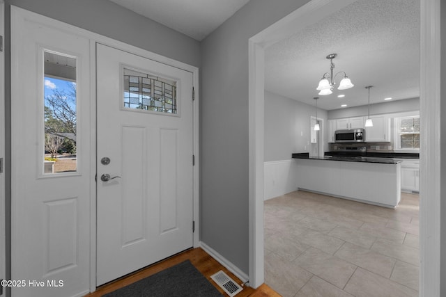 foyer with a wealth of natural light, visible vents, a notable chandelier, and a textured ceiling