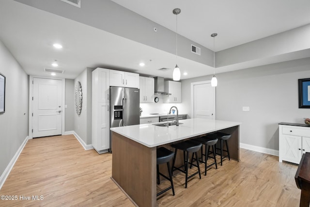 kitchen with a center island with sink, sink, white cabinetry, wall chimney range hood, and hanging light fixtures