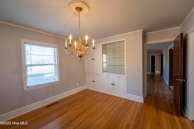 unfurnished dining area with hardwood / wood-style flooring, ornamental molding, and an inviting chandelier