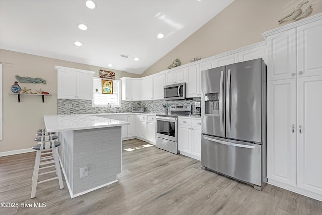 kitchen with tasteful backsplash, white cabinets, lofted ceiling, a kitchen breakfast bar, and stainless steel appliances