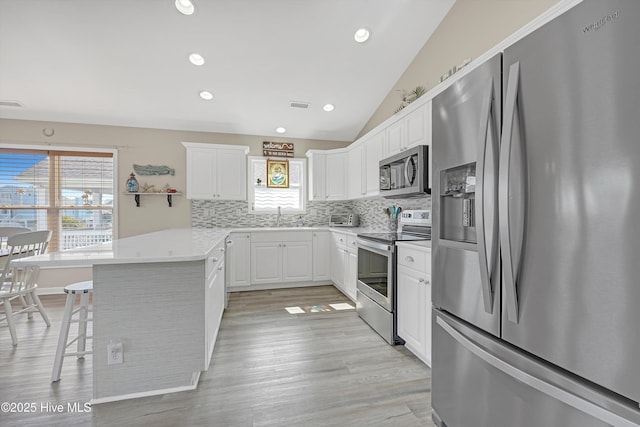 kitchen with appliances with stainless steel finishes, vaulted ceiling, a sink, a peninsula, and a kitchen breakfast bar