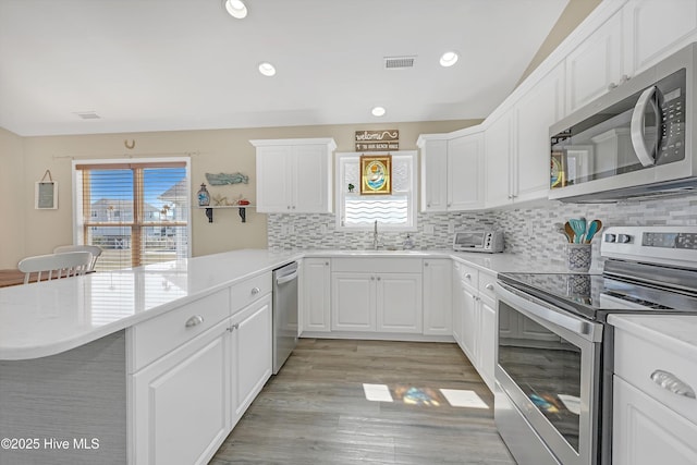 kitchen featuring stainless steel appliances, light countertops, visible vents, a sink, and a peninsula