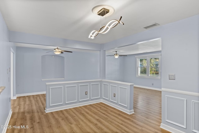 spare room featuring ceiling fan with notable chandelier and light wood-type flooring