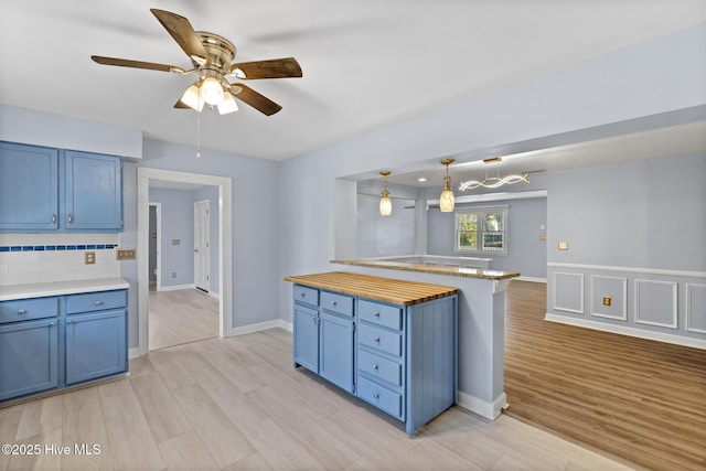 kitchen featuring blue cabinetry, decorative backsplash, light hardwood / wood-style floors, and pendant lighting